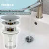 A close-up view of a chrome pop-up drain assembly for a sink, with water flowing into the sink and around the drain. Produktbild-Vorschau