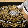 A close-up view of a rug with an intricate oriental pattern in gold and white on a black background. A woven basket with a striped towel is partially visible on the right side. Produktbild-Vorschau