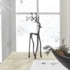 A decorative metal deer figurine stands on a wooden table in front of a window with a snowy view. Produktbild-Vorschau