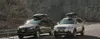 Two SUVs with roof boxes are parked on the side of a road with a rocky mountain in the background. Produktbild-Vorschau