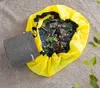 A yellow toy storage bag filled with building blocks is spread open on a carpeted floor, with a gray mat next to it. Podgląd zdjęcia produktu
