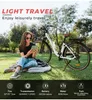 A woman is sitting on the grass next to an electric bicycle in a park. Produktbild-Vorschau