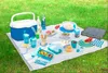 A picnic spread on a lawn with a cooler, food containers, drinks, and plates. Anteprima dell’immagine prodotto