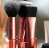 A close-up shot of three makeup brushes with rose gold handles and black bristles, standing in a clear acrylic holder. Produktbild-Vorschau