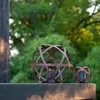 Two spherical garden lanterns with candles inside, placed on a wooden surface with a blurred green background of trees. Voir les images du produit