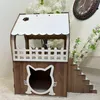 A wooden cat house with a white roof and fence, decorated with a paw print and a cat face cutout. It is placed on a white surface with white flowers in the background. Produktbild-Vorschau