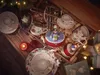 A collection of Christmas-themed porcelain items, including plates, cups, and decorative figurines, arranged in a wooden crate with festive lights. Produktbild-Vorschau