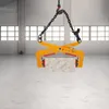 A stone clamp is suspended by chains, holding a rectangular stone block in a warehouse-like setting. Voir les images du produit