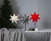 Three star-shaped lamps are displayed on a table in front of a Christmas tree and a gray wall. Podgląd zdjęcia produktu