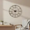 A wall clock is mounted on a wall above a shelf with books and a plant, next to a chair with a blanket. Voir les images du produit