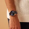 A close-up shot of a person's wrist wearing a blue-faced watch with a rose gold casing and a navy leather strap, with a textured white sweater visible in the background. Voir les images du produit