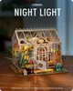 A miniature greenhouse model with lights on, displayed on a wooden surface. Podgląd zdjęcia produktu