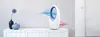 A white stand fan is shown on a white cabinet, with blue and pink air currents emanating from it. Produktbild-Vorschau