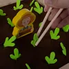 A close-up of a wooden toy garden game with a farmer figurine and green felt sprouts being picked with chopsticks. Voir les images du produit