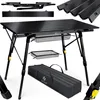 A black foldable camping table with its accessories, including a carrying bag and storage baskets, displayed against a white background. Produktbild-Vorschau