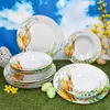 Easter-themed dinnerware set with bunny and floral motifs displayed on a grassy surface with a sky background. Náhled obrázku produktu