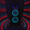A black trolley speaker with blue lights on top and green lights around the speakers, set against a dark background with red and blue light effects. Voir les images du produit