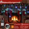 Christmas lights with snowflake decorations hanging over a fireplace with stockings. Produktbild-Vorschau