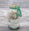 A glass jar filled with decorative items and tied with a ribbon, set against a wooden background. Podgląd zdjęcia produktu