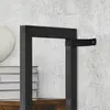 A close-up view of a black metal frame shelf with a fabric strap attached to it, set against a textured gray and white wall. A stack of books and a white decorative object are partially visible on the left. Produktbild-Vorschau