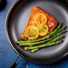 A close-up shot of a cooked salmon fillet with lemon slices and asparagus in a hexagonal-patterned frying pan. Náhled obrázku produktu