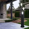 A modern outdoor patio with a stone fireplace, paved flooring, and landscaping, featuring a set of three black bollard lights with white illuminated tops. Produktbild-Vorschau