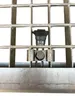 A close-up view of a metal grate with a bolt and clamp assembly. Anteprima dell’immagine prodotto