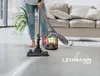 A person is using a vacuum cleaner in a living room with a sofa and plant in the background. Náhled obrázku produktu