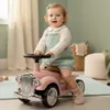 A baby is sitting on a pink ride-on car in a room. Produktbild-Vorschau
