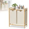 A two-compartment laundry basket with a bamboo frame and a shelf on top, displayed against a white background. Several bottles of soap and a potted plant are arranged on the shelf. Voir les images du produit