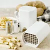 A white potato slicer with a grid of blades is shown in the foreground, next to cut potato pieces. In the background, there are salt and pepper shakers, a plate of french fries, and whole potatoes in a basket. Produktbild-Vorschau