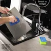 A person is cleaning a cutting mat under a faucet in a kitchen sink. Produktbild-Vorschau