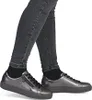 A person wearing dark jeans and black socks is shown from the knees down, wearing silver sneakers. Náhled obrázku produktu
