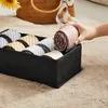 A hand is putting a rolled-up tie into a black organizer box filled with other ties. Produktbild-Vorschau