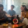 Three people are sitting on a couch and laughing while holding microphones connected to a karaoke machine. Produktbild-Vorschau