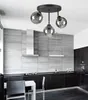 A modern kitchen with a sleek black countertop, dark cabinets, and a stainless steel range hood. A contemporary chandelier with three glass globes hangs above a white table with chairs. Produktbild-Vorschau