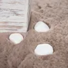 A close-up view of a beige, fluffy rug with three white stones partially embedded in it. A corner of a distressed wooden box is visible in the upper left. Produktbild-Vorschau