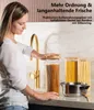 A woman is placing a lid on a tall glass jar filled with spaghetti, with other jars of pasta and a pot on a kitchen counter. Produktbild-Vorschau