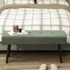 A green bench sits in front of a bed with plaid bedding. Produktbild-Vorschau