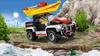 A toy SUV with a kayak on top is driving on a rocky path near a river, with a sunny sky and distant city skyline. Produktbild-Vorschau