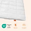 A close-up view of a white quilted blanket with several certification icons and text at the bottom. Produktbild-Vorschau