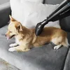 A dog is lying on a gray couch while a vacuum cleaner attachment is being used on its fur. Voir les images du produit