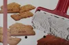 A baking roller with a patterned surface is shown next to several Speculoos cookies. Produktbild-Vorschau