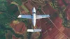 An aerial view of a small white airplane flying over agricultural fields. Produktbild-Vorschau