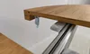 A close-up view of the edge of a wooden table with a metal sliding mechanism underneath. Náhled obrázku produktu