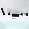 A black bathtub faucet set with multiple controls and a waterfall spout is installed on the edge of a white bathtub. Produktbild-Vorschau