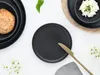 A table setting with black plates, a bread roll, and a knife. Náhľad obrázku produktu