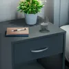 A close-up of a dark gray nightstand with a drawer, a plant in a white pot, a stack of notebooks with a pen, and a glass of water. Produktbild-Vorschau