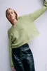 A woman wearing a green sweater and black pants against a white background. Produktbild-Vorschau