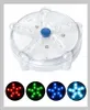 A clear product shot of a round, clear plastic device with blue accents and multiple LED lights, shown above four circular examples of the device emitting red, green, blue, and cyan light. Náhled obrázku produktu